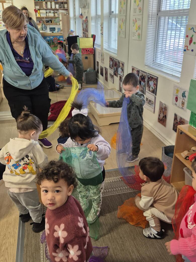 A teacher trailing a length of blue chiffon through the room while children reach for scarves of their own.