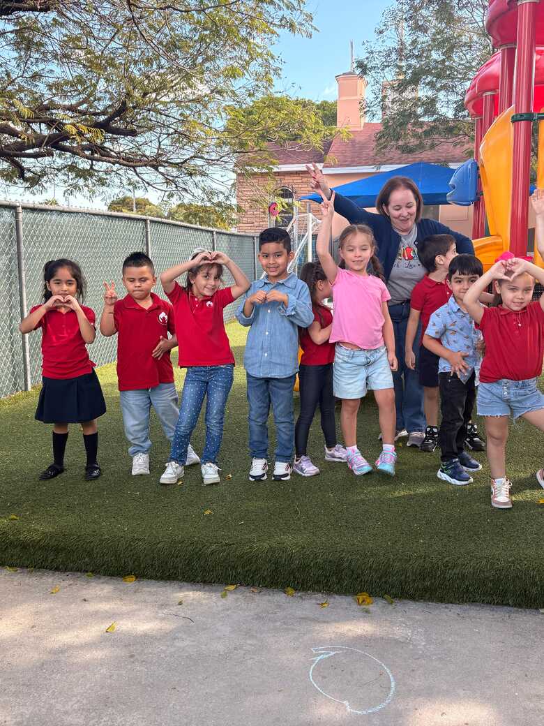 A class standing together on the turf outside, making heart shapes with their hands.