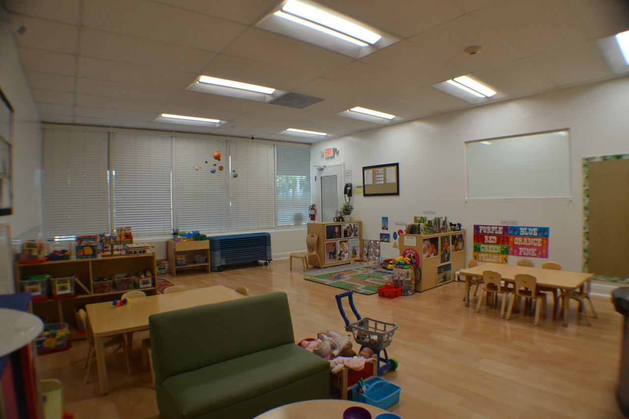 A spacious classroom with wood floors, a small couch, and low wooden tables.
