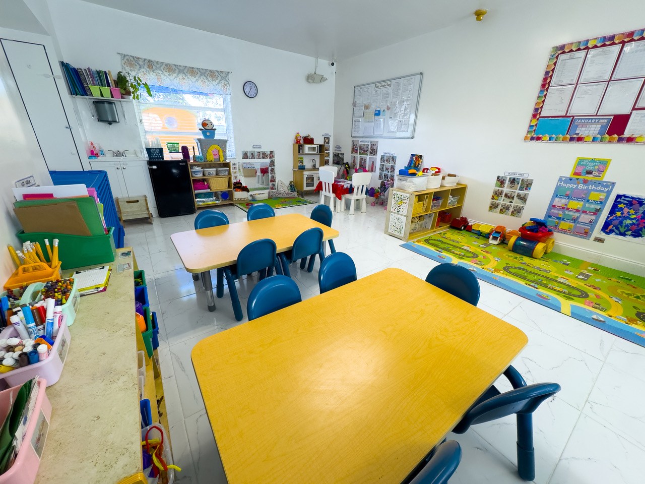 A classroom with a yellow worktable, blue chairs, and a colorful alphabet rug.