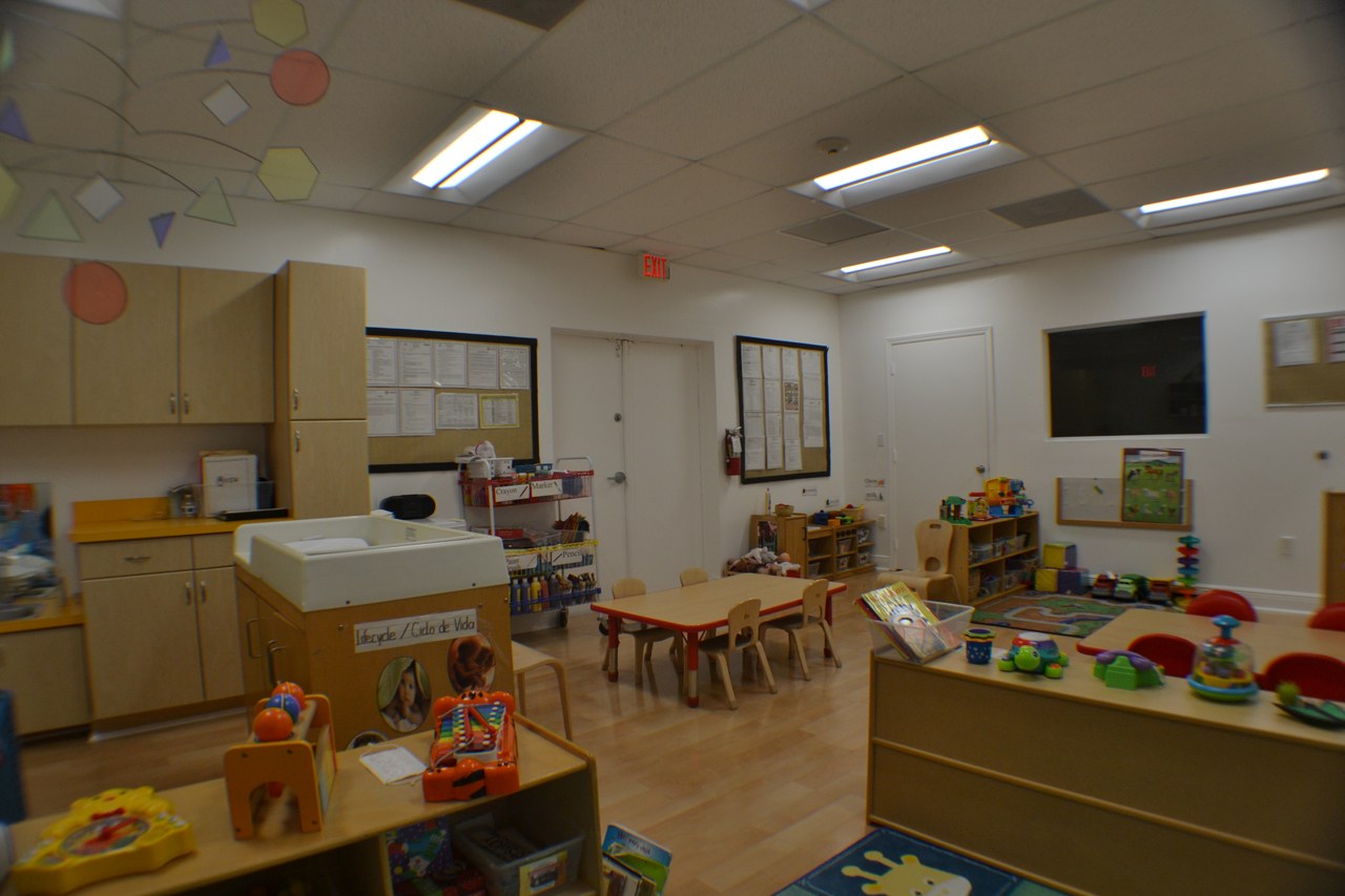 A classroom with wooden toy shelves, low tables, and cabinets along the wall.