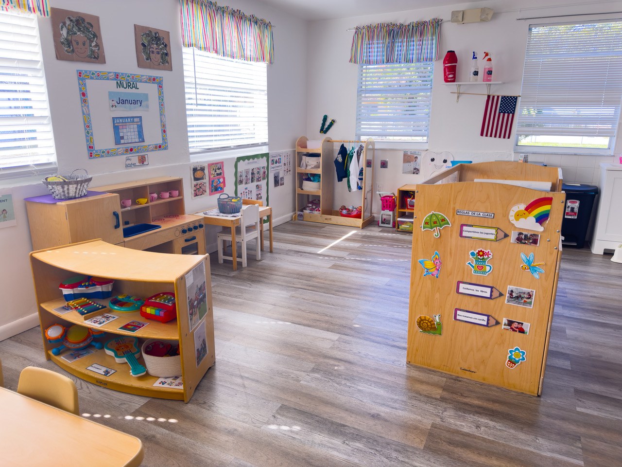 A classroom with wood floors, open toy shelves, and a standing activity board.