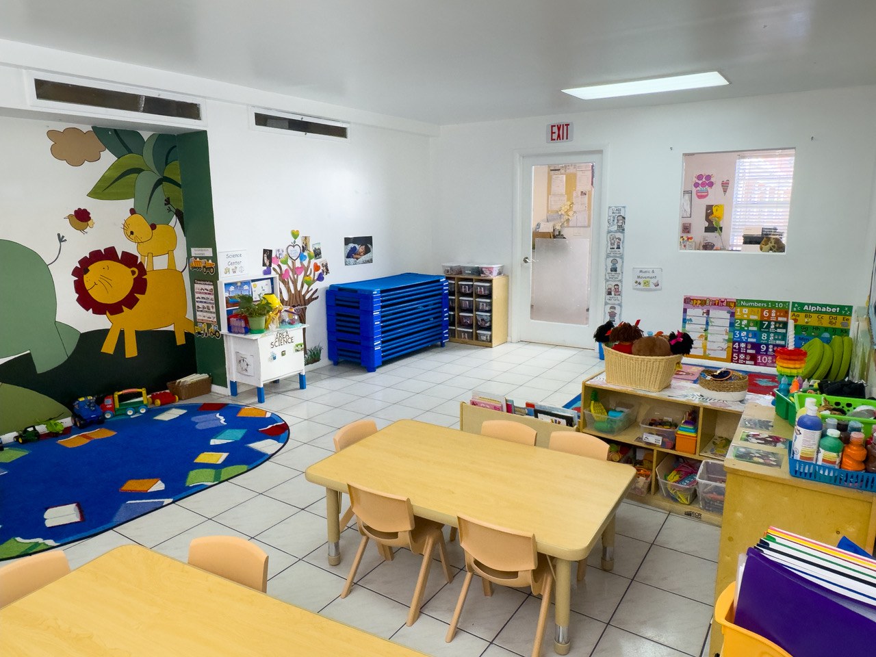 A classroom with a painted jungle mural, tile floors, and blue storage drawers.