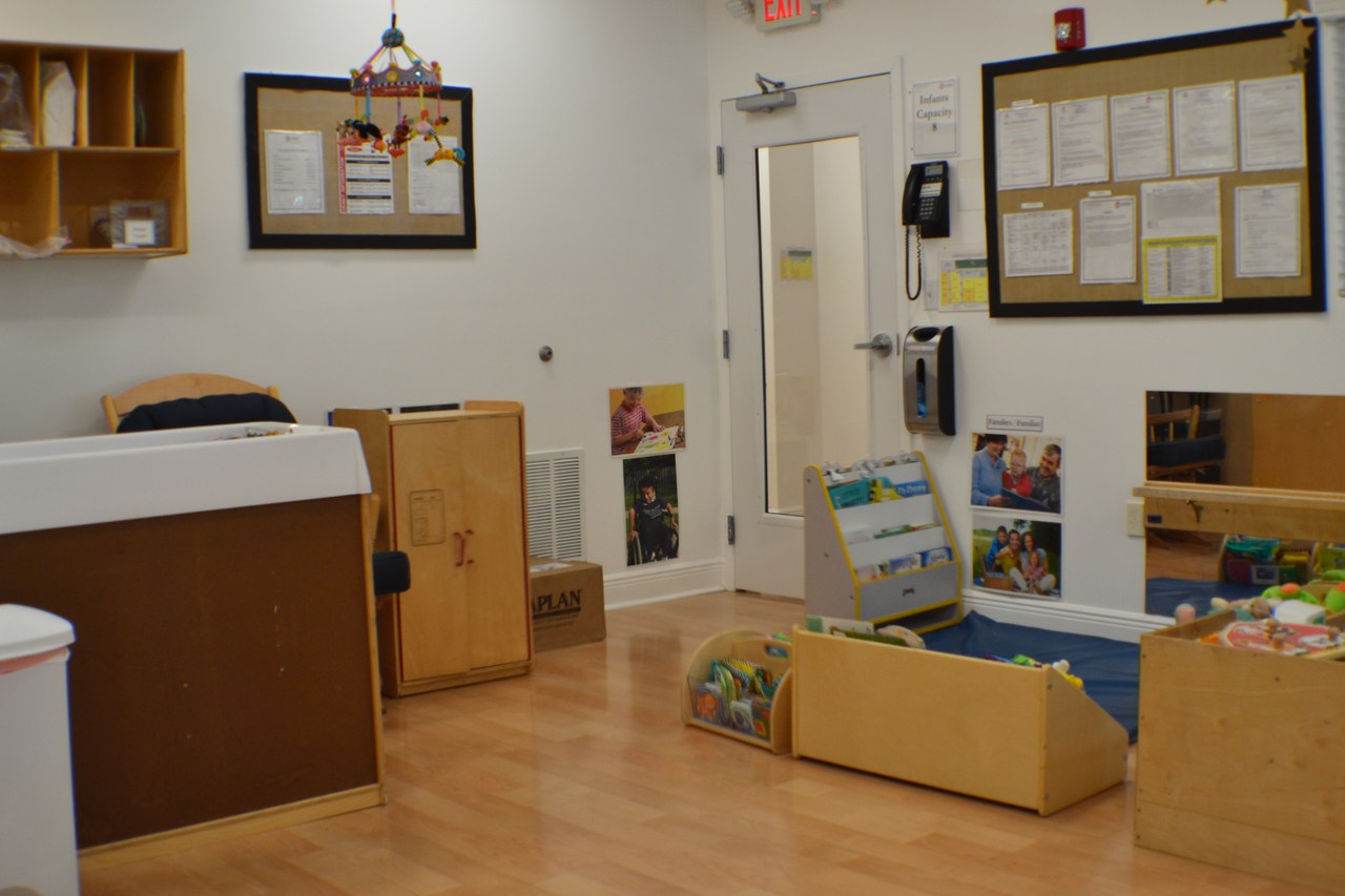 A classroom with wood floors, framed noticeboards, and labelled storage bins.