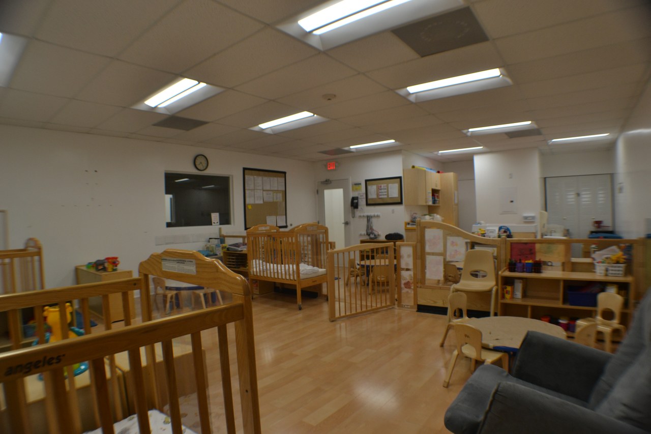 An infant room with wooden cribs and low shelves on a wood floor.