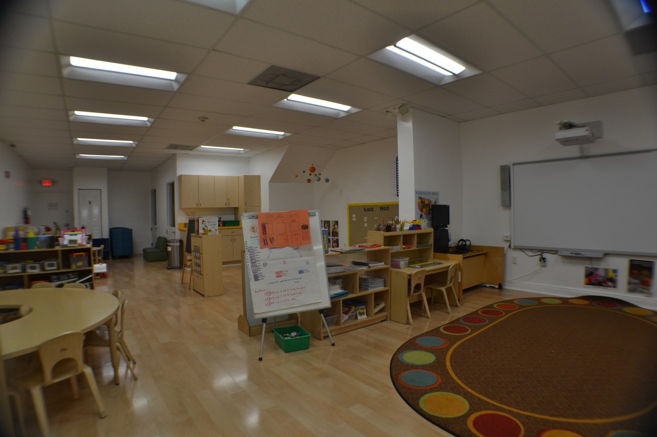 A classroom with a patterned rug, a painting easel, and low tables.